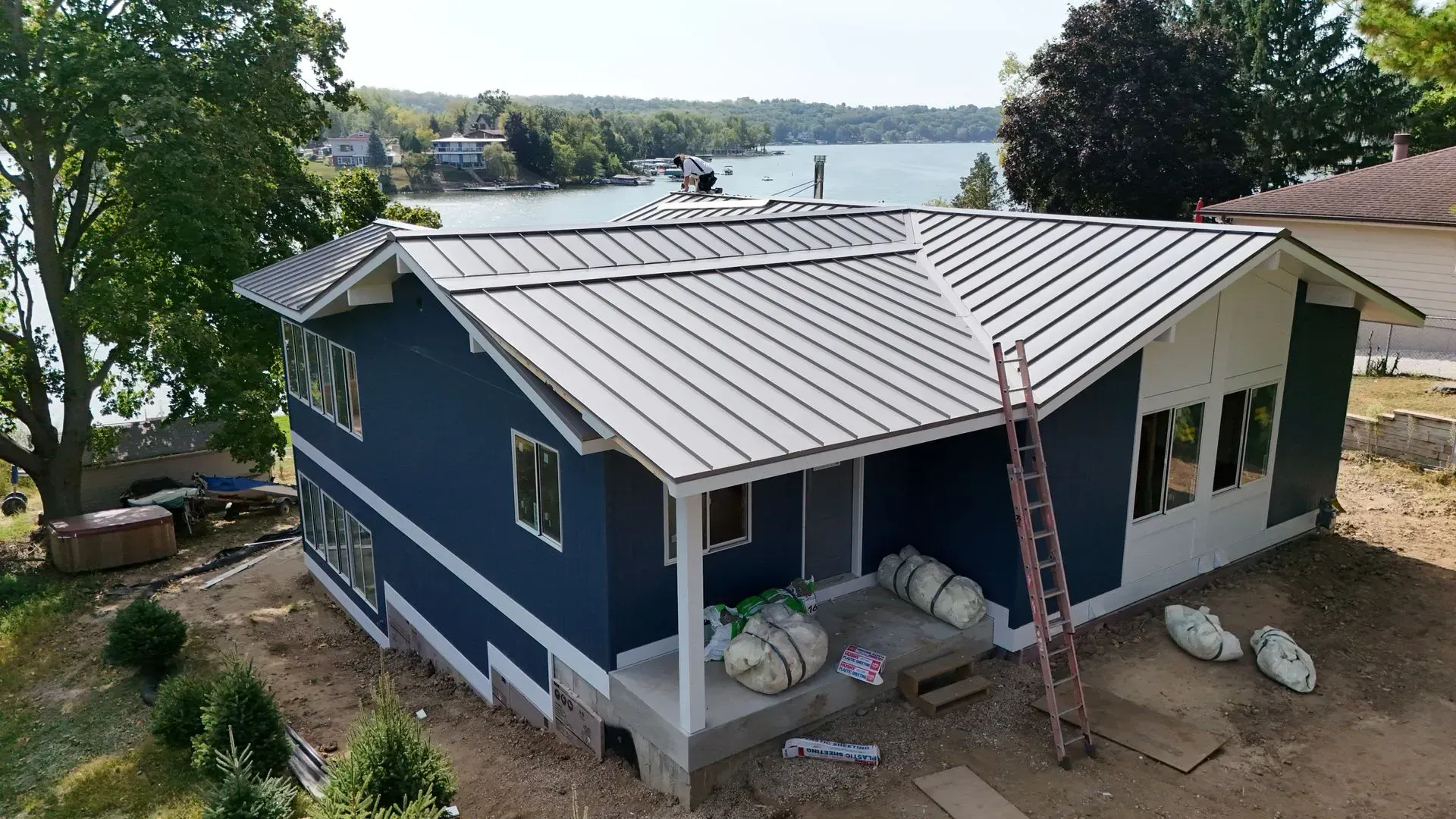 Blue house with metal roof under construction by a lake.