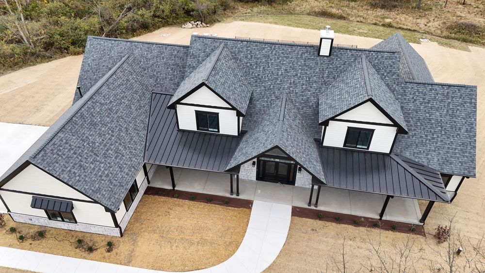 Aerial view of a modern farmhouse with a dark roof and white trim. Black-framed windows, and porch with pillars.
