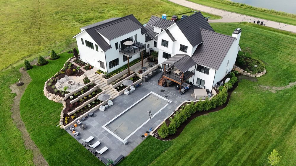 White house with dark roof and large patio, surrounded by green grass and landscaping.