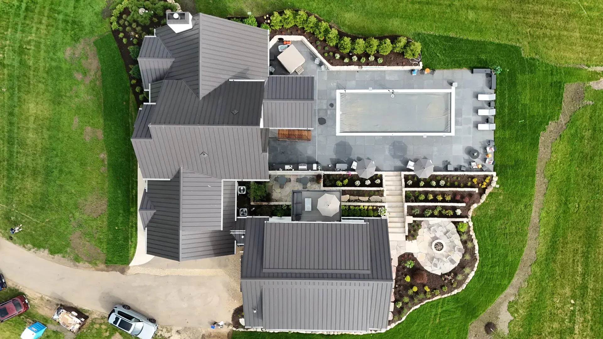 Aerial view of a modern home with a pool, patio, fire pit, and surrounding greenery.
