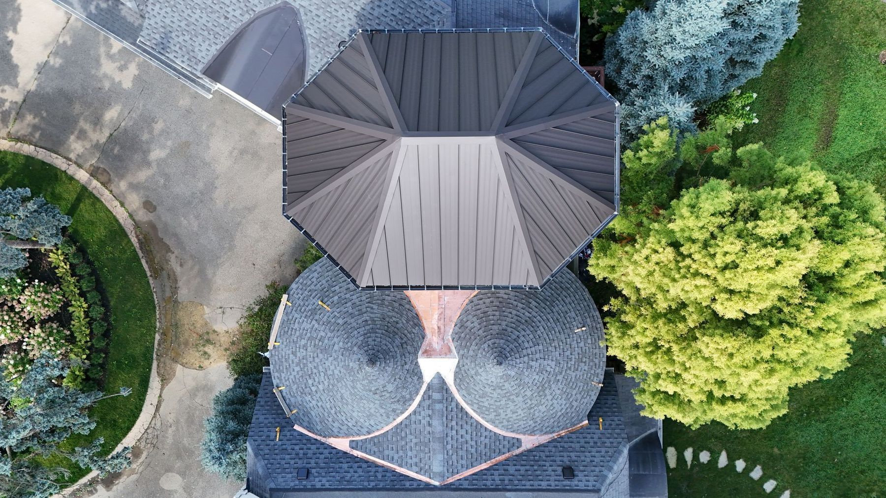 Overhead view of a house with a multi-faceted gray roof, two rounded sections, and surrounding greenery and driveway.