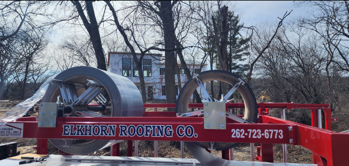 A red roofing machine with rolls of metal. "Elmurn Roofing Co." and phone number on the side.