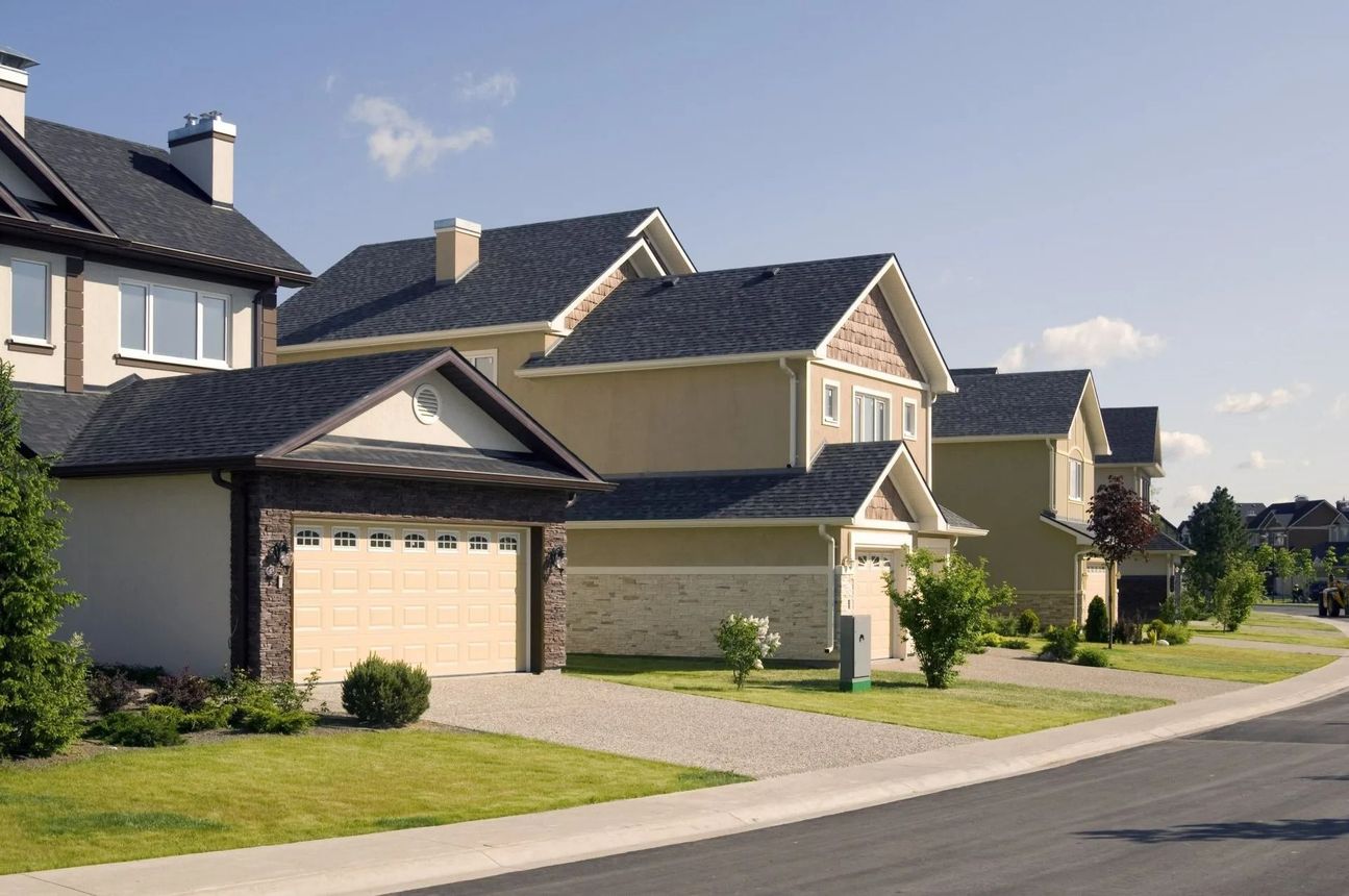 Row of suburban houses with matching dark roofs and beige exteriors, on a sunny street.