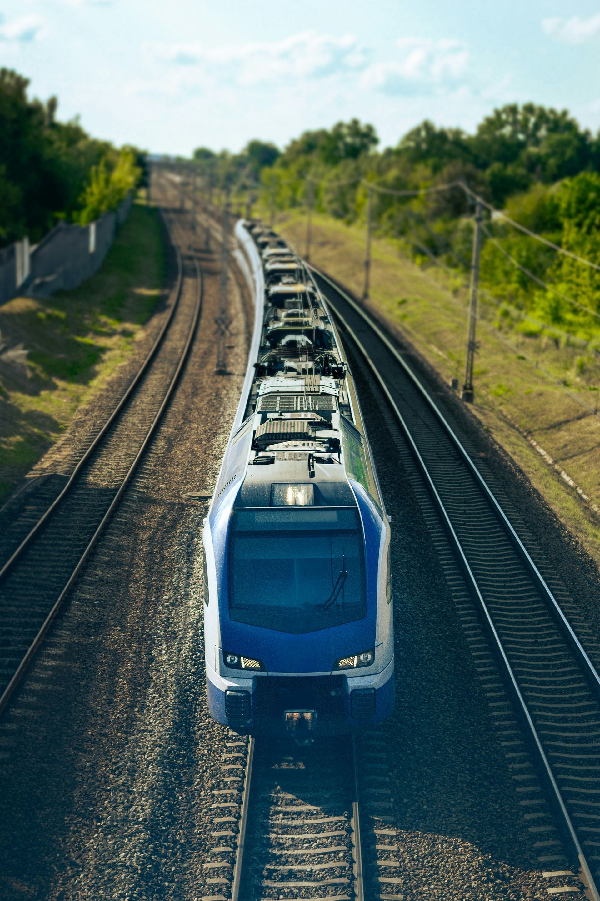 Train on tracks, viewed from above, traveling through a rural area. Coloured photo.