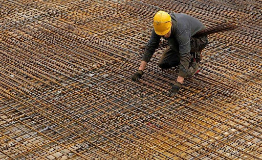 Construction worker laying rebar in an outdoor setting, wearing a yellow hard hat.