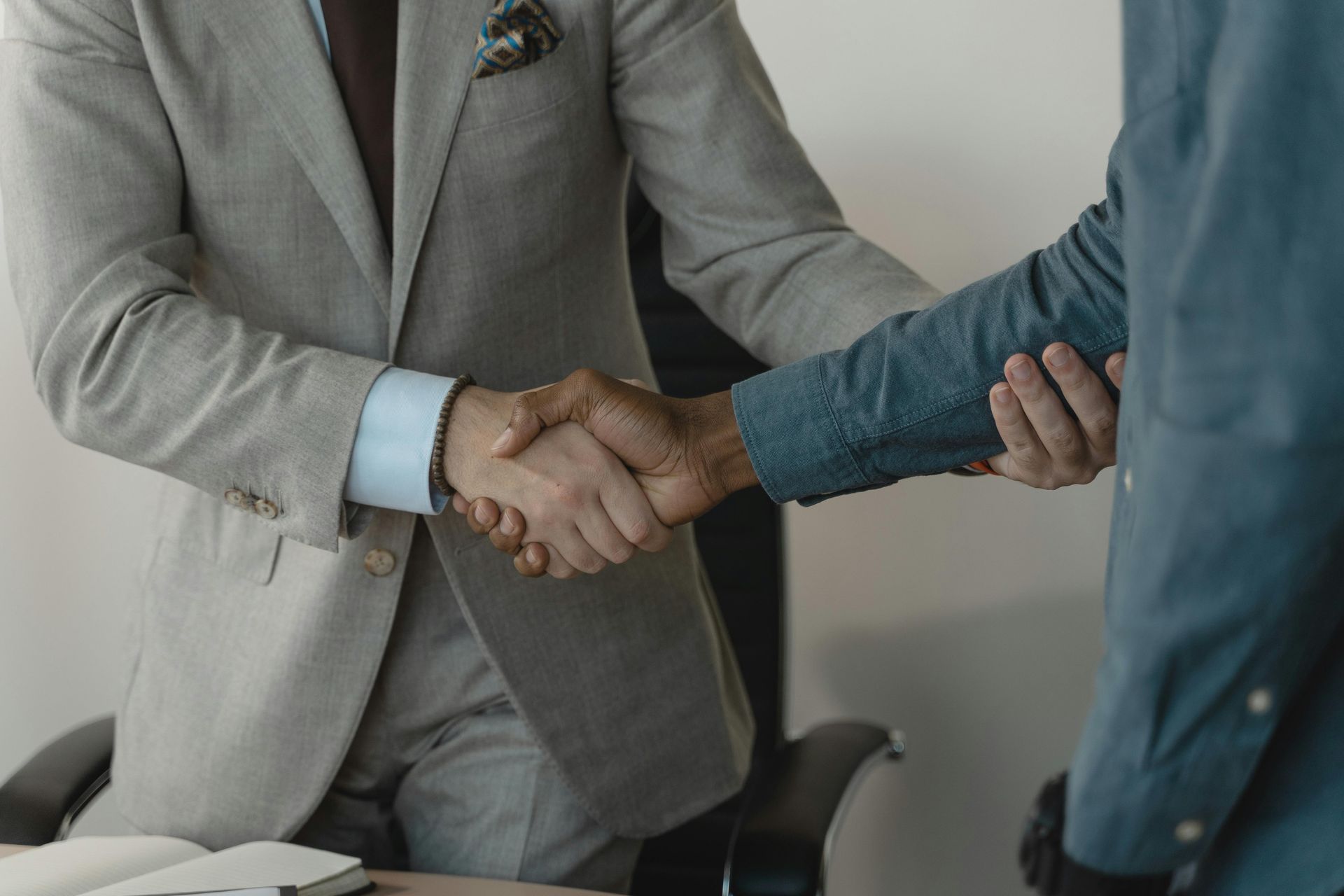 Two men in suits shaking hands in an office setting.
