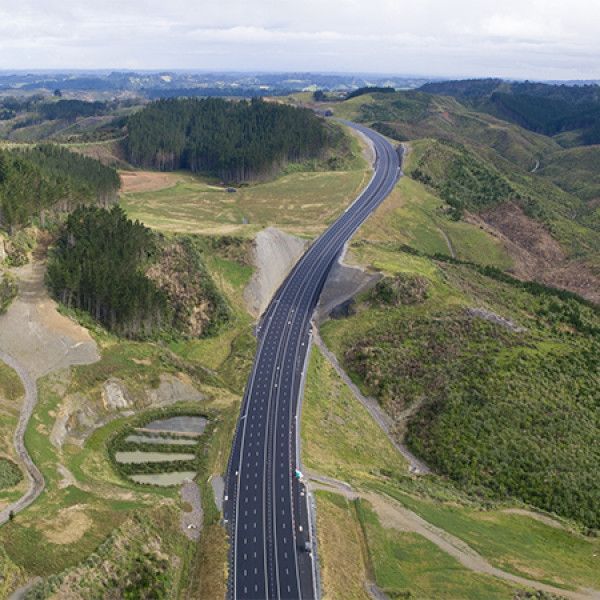 Elevated view of a multi-lane highway winding through a green rural landscape, with hills and patches of forest.