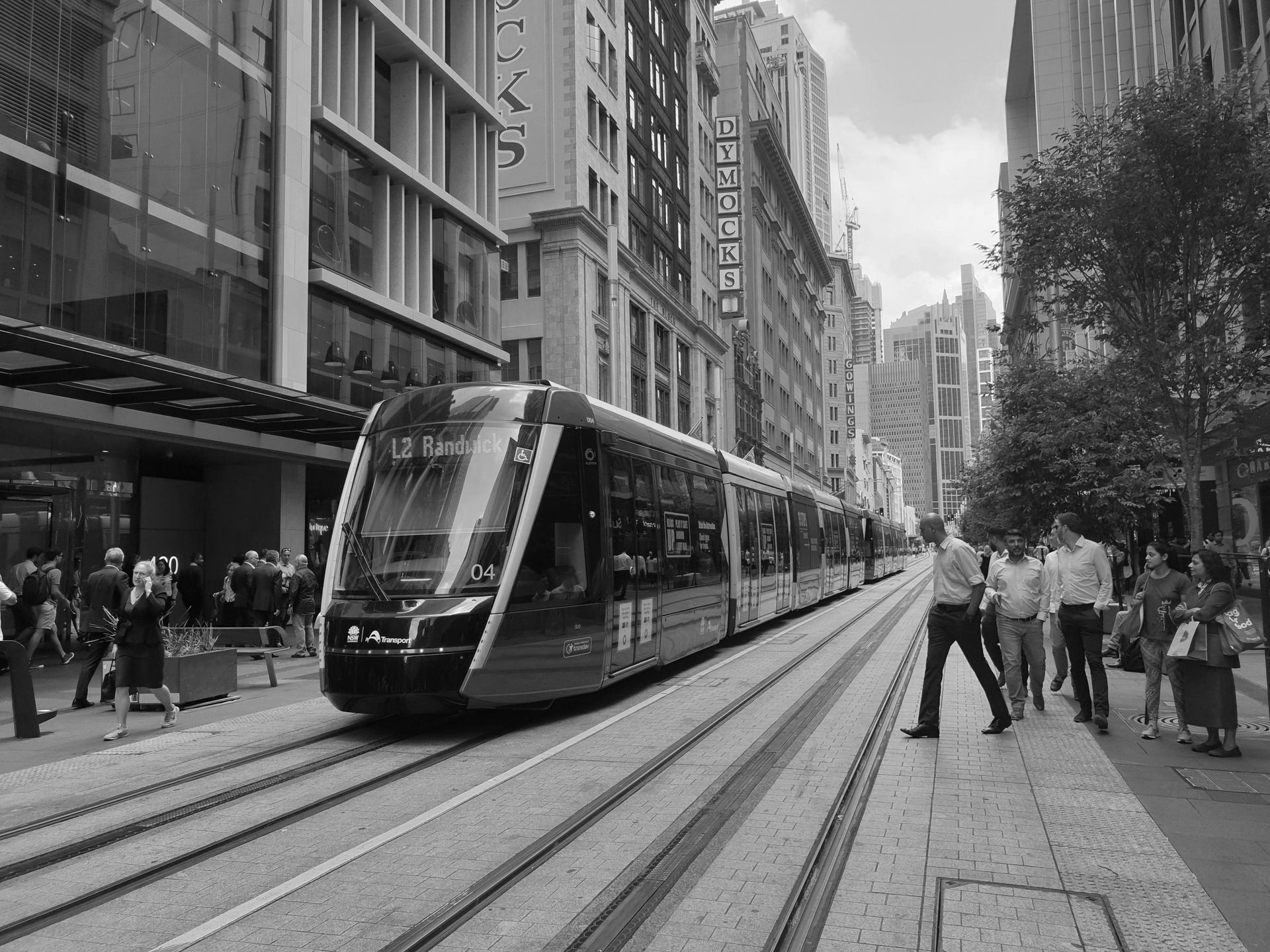 A red and black tram travels down a city street with pedestrians and tall buildings in Sydney, Australia.