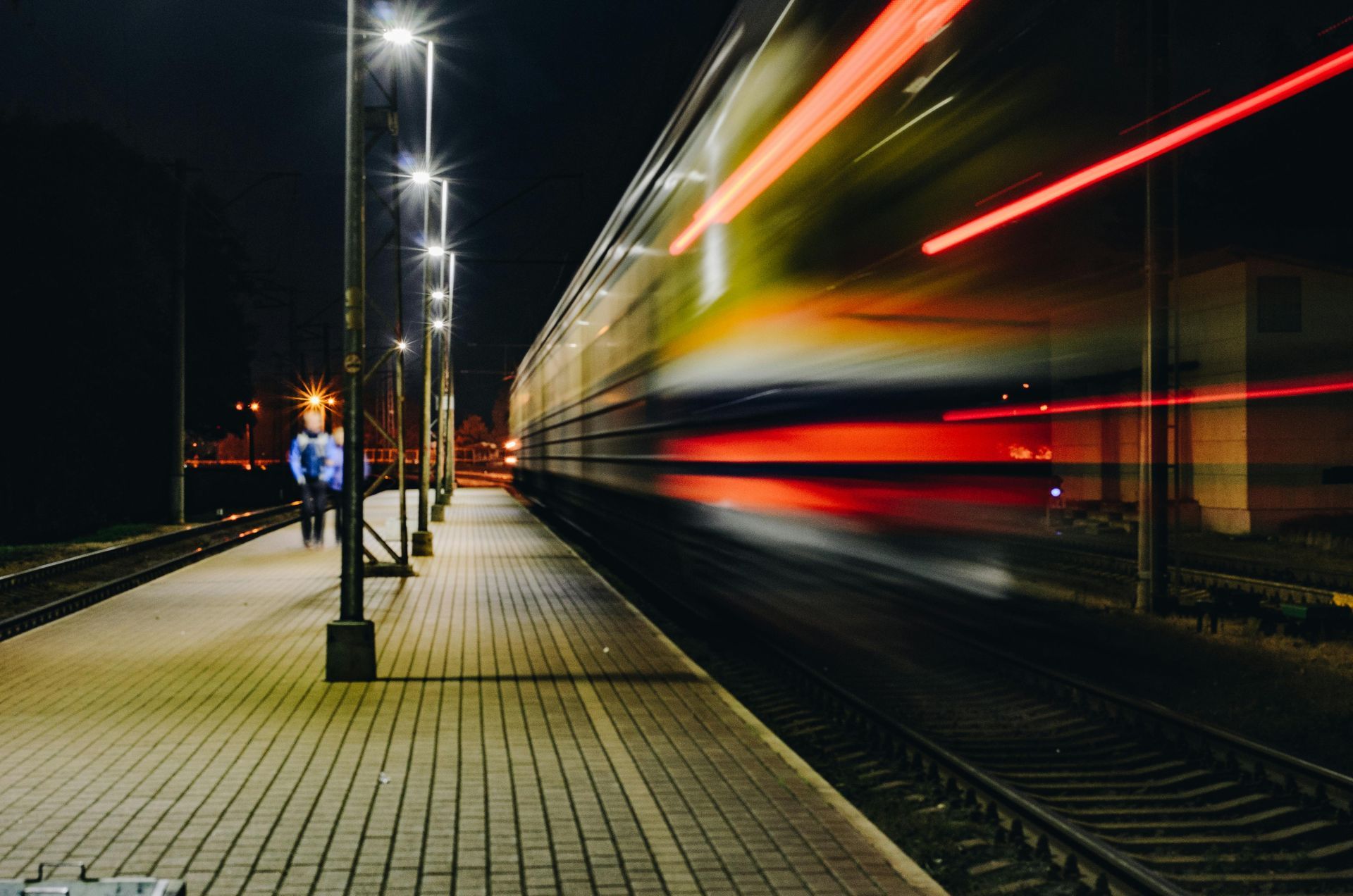 Train speeding past a lit-up platform at night, blurring red and yellow lights.