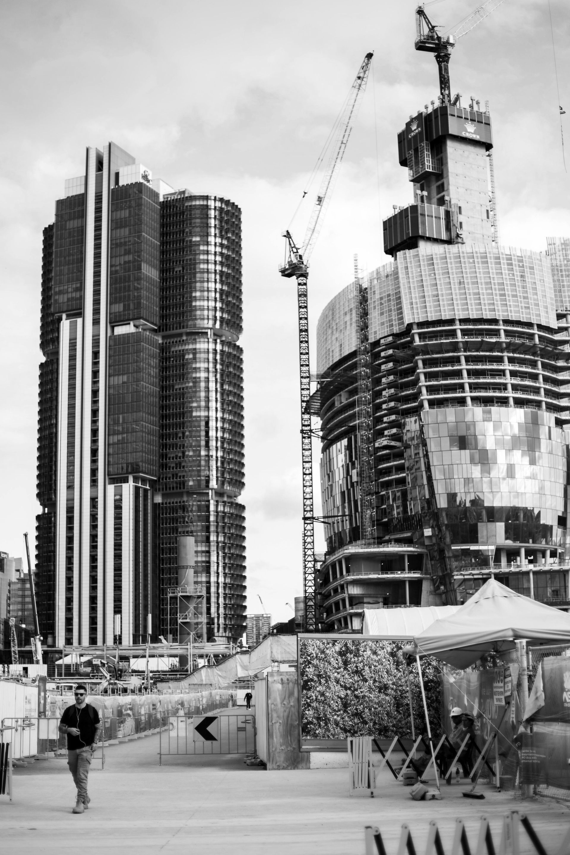 Construction site with skyscrapers, cranes, and a person walking on a path in black and white.