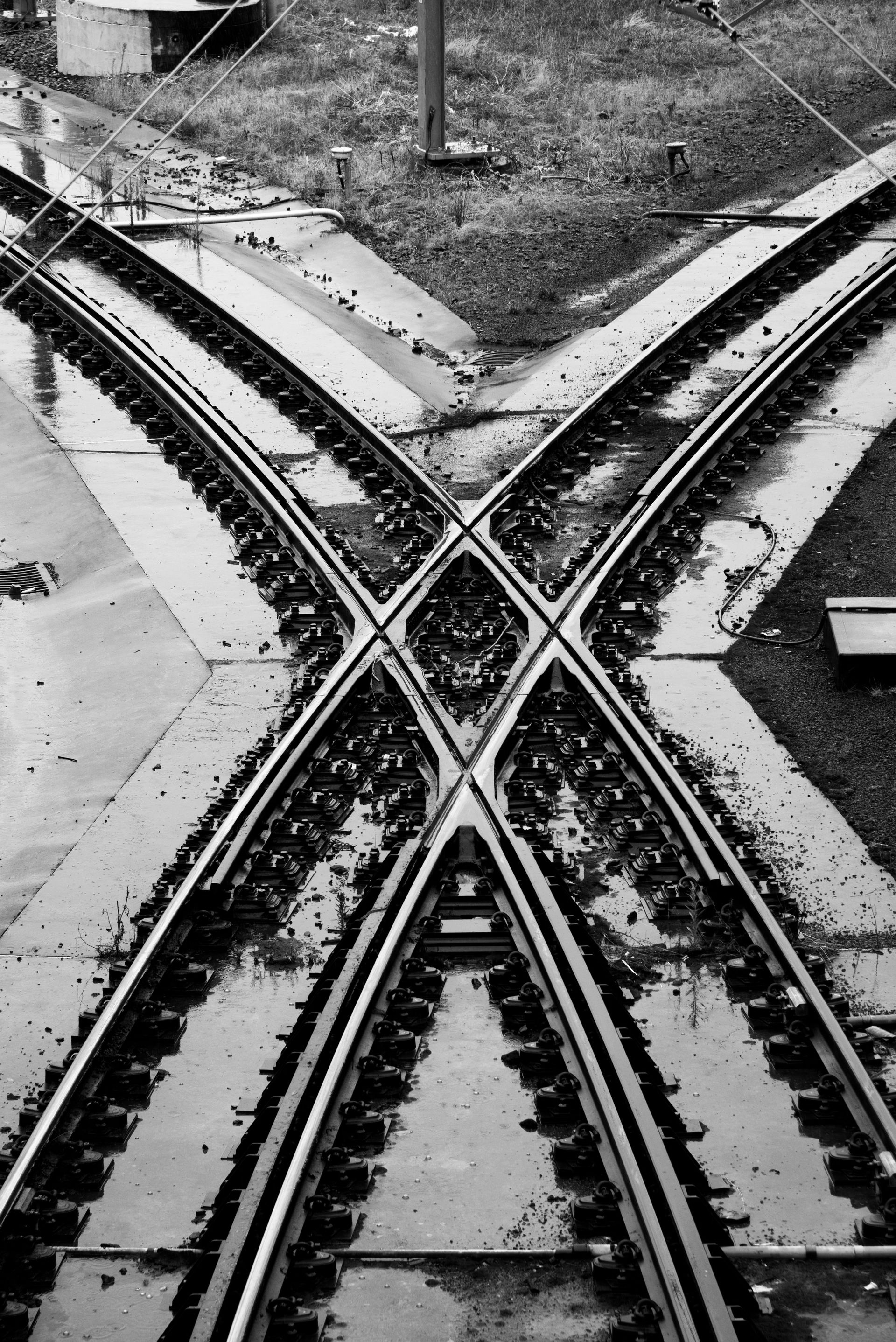 Railroad tracks crossing in an X shape, viewed from above, in black and white.