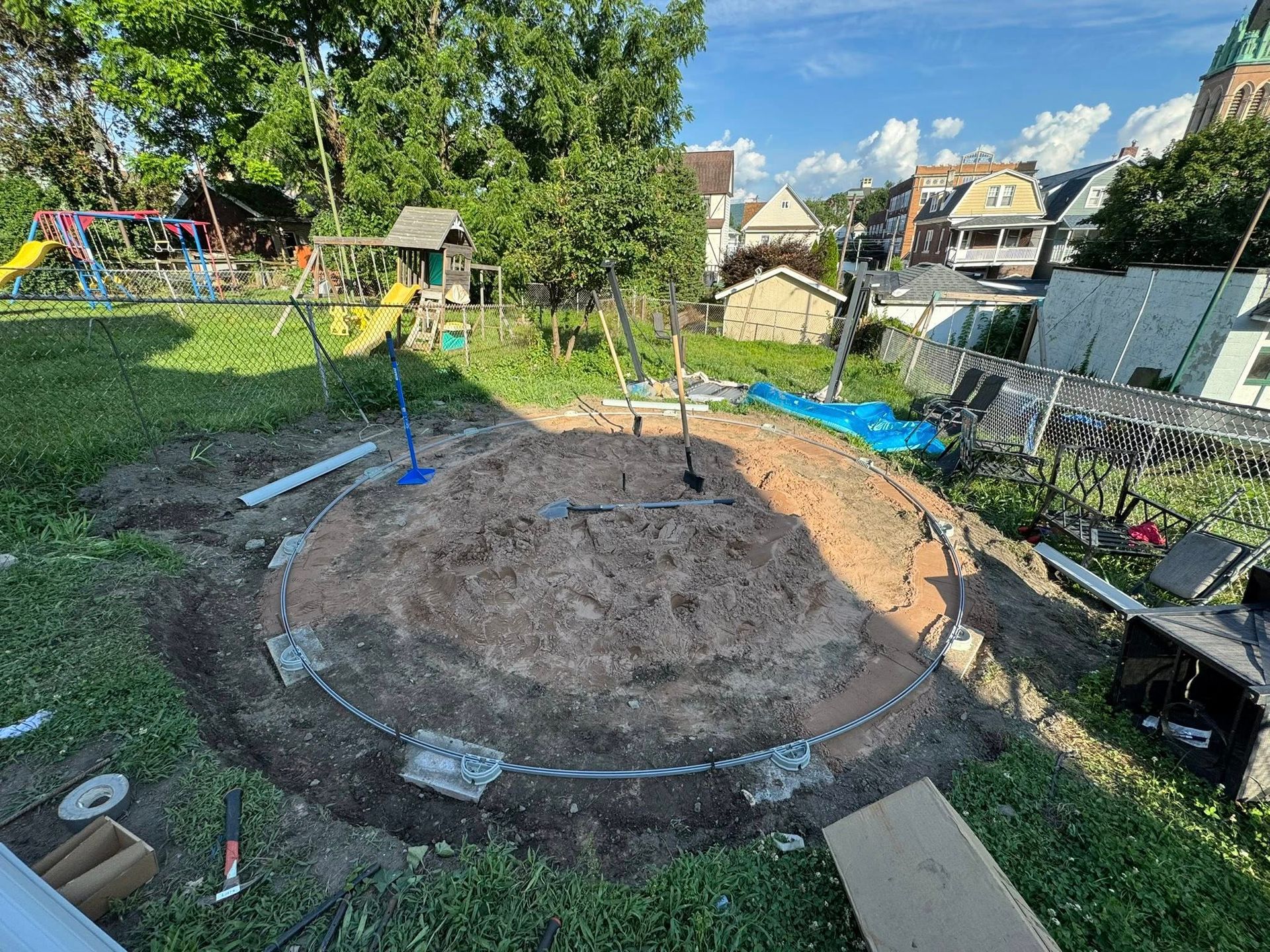 A partially excavated backyard, prepped for a circular pool, with building materials and equipment scattered around.