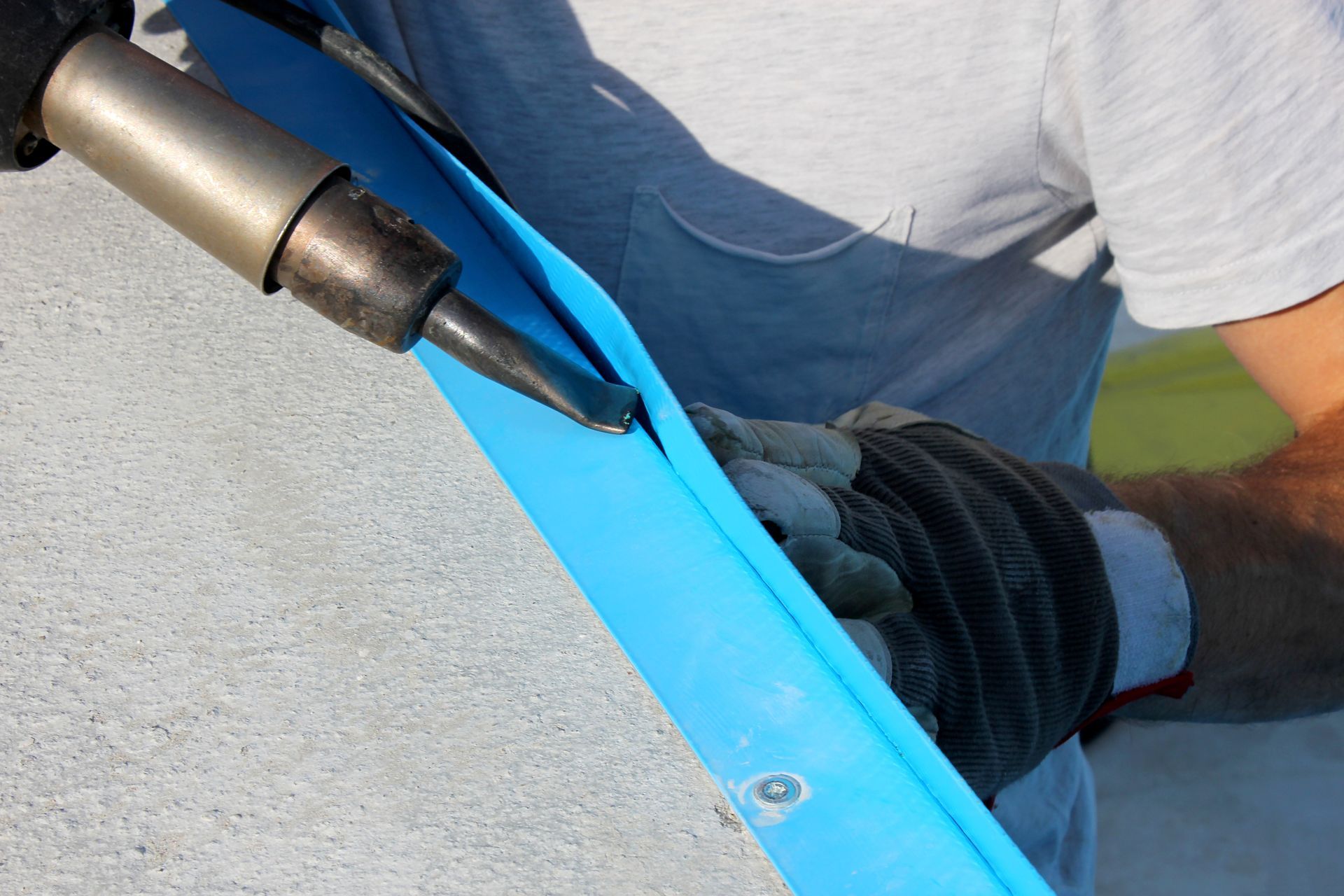 A person welding blue material with a handheld tool; the setting is outdoors.