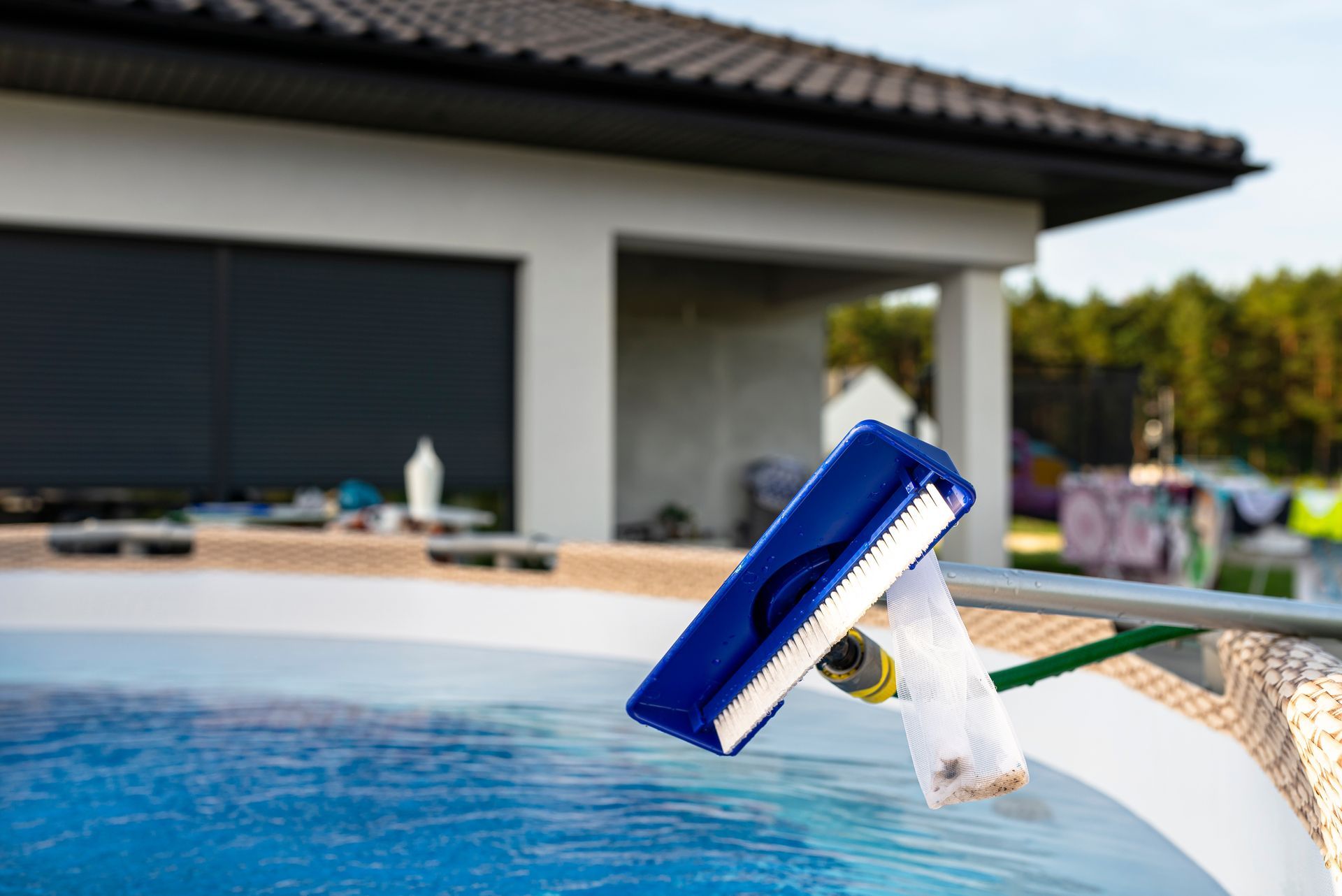 Pool cleaner brush in a pool; a house is in the background.