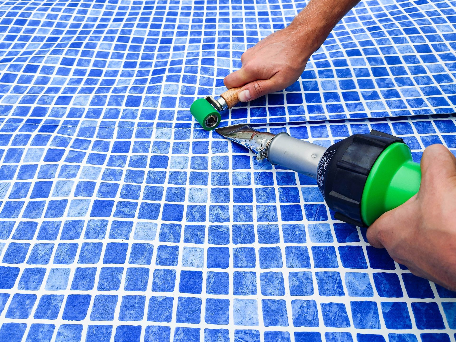 Hands welding a pipe on a blue tiled surface with a green tool.