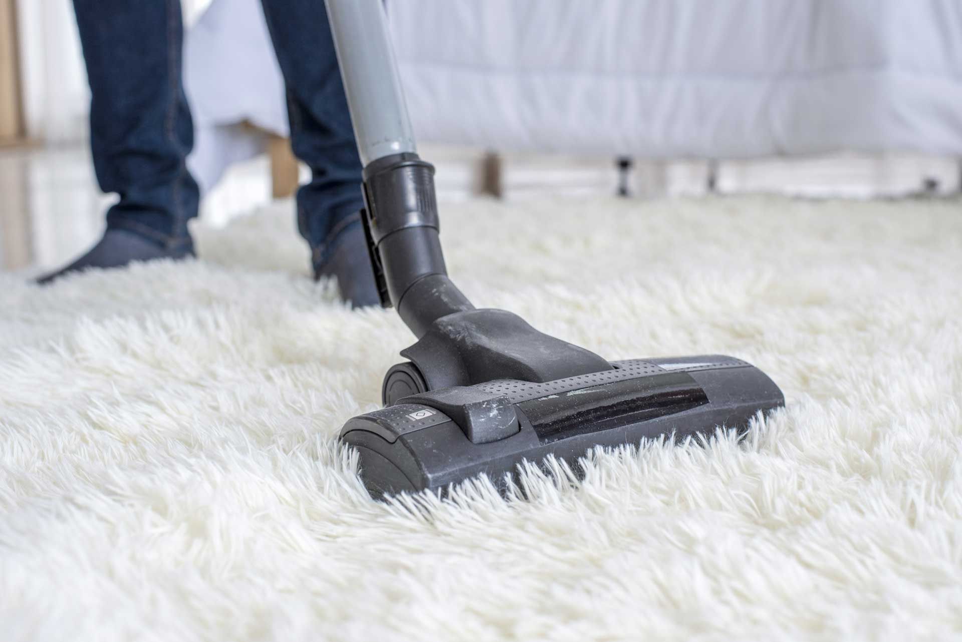 Person vacuuming a fluffy, white rug in a bedroom.