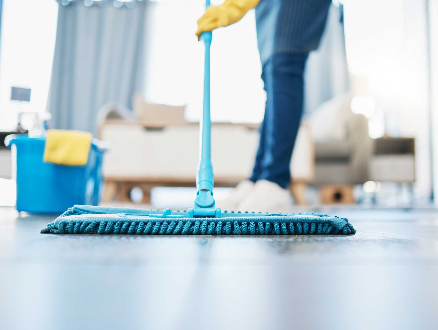 Person mopping a floor with a blue mop; cleaning supplies in a blue bucket in the background.