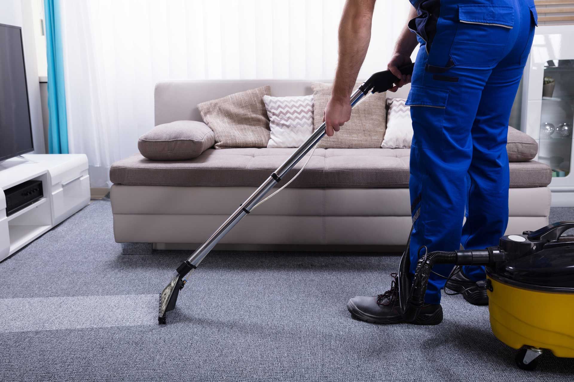 Person in blue overalls vacuuming carpet in a living room. Person in blue overalls vacuuming carpet in a living room.