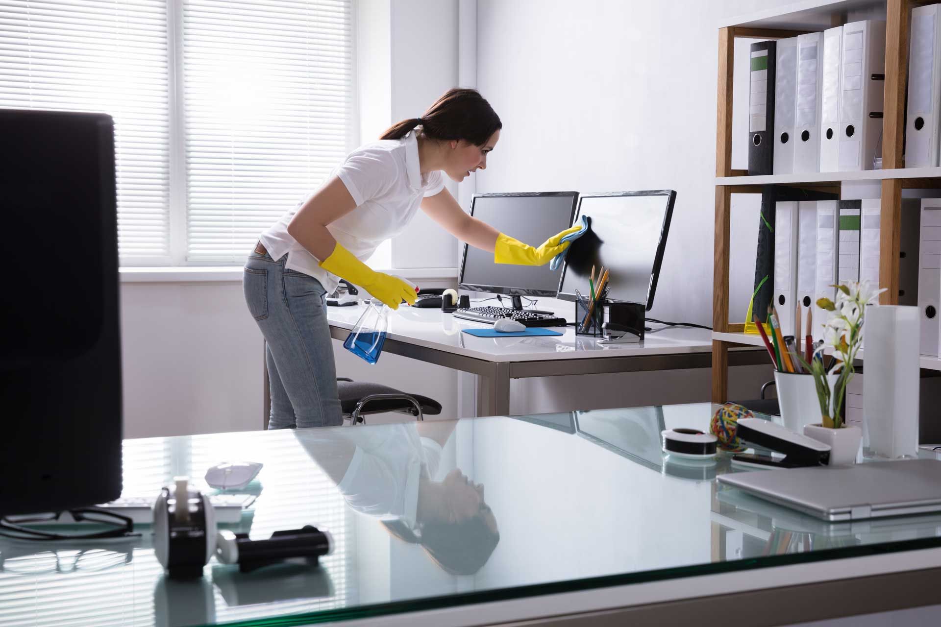 Woman in yellow gloves cleaning a computer monitor in an office.