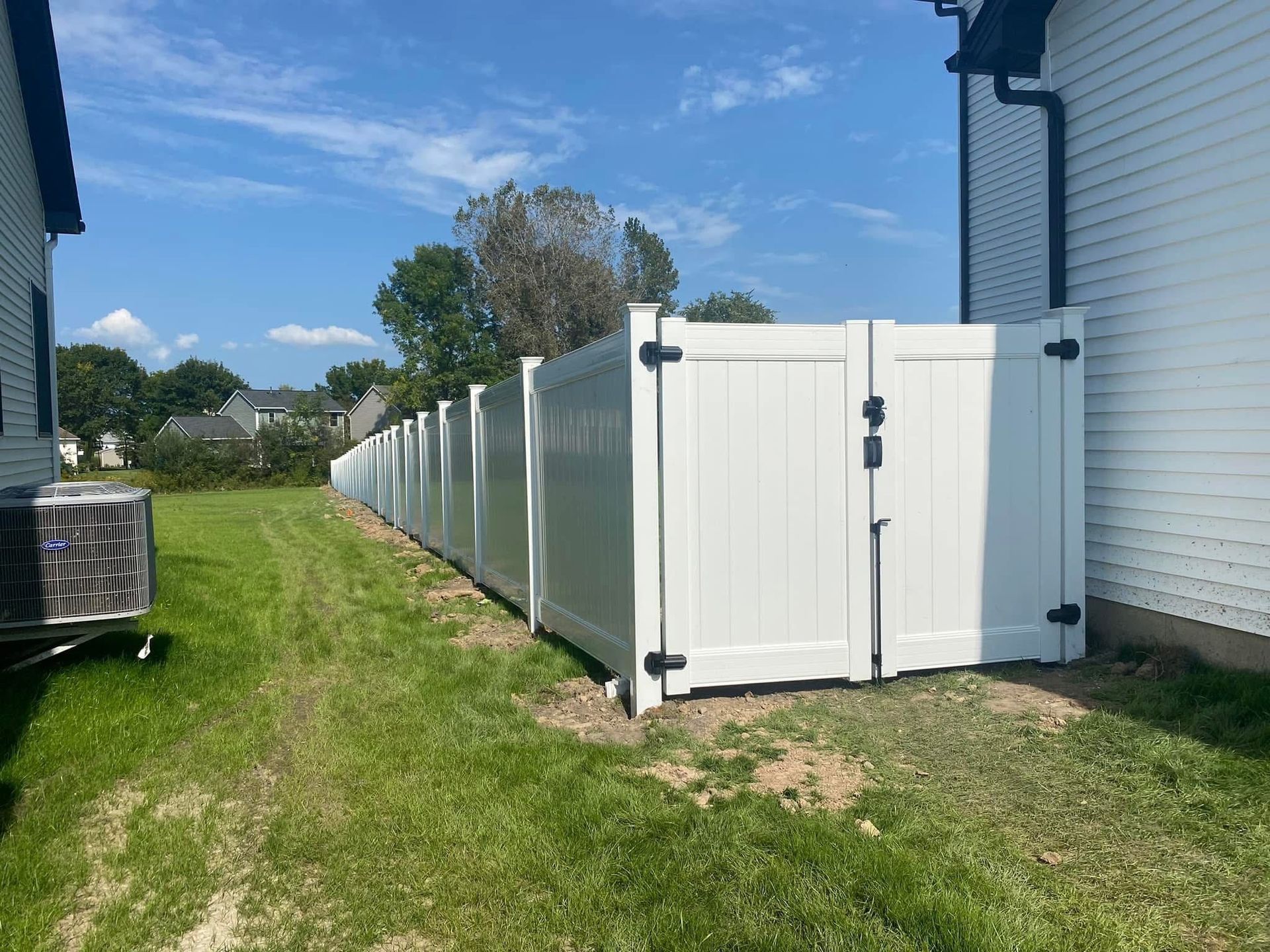 A white fence with a gate in the backyard of a house.