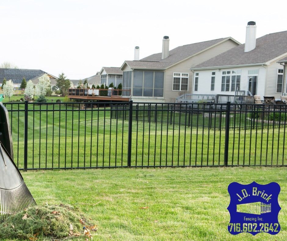 A black fence surrounds a lush green yard in front of a house