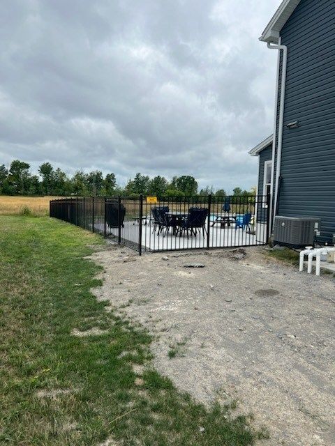 Black metal fence surrounding a patio with outdoor furniture next to a house with blue siding.
