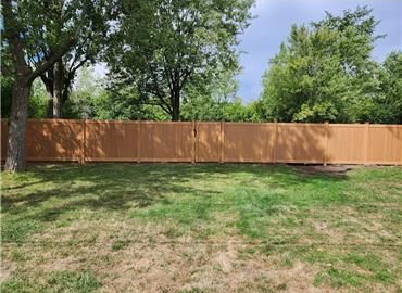 Brown wooden fence in a grassy yard, trees in the background, partly cloudy sky.