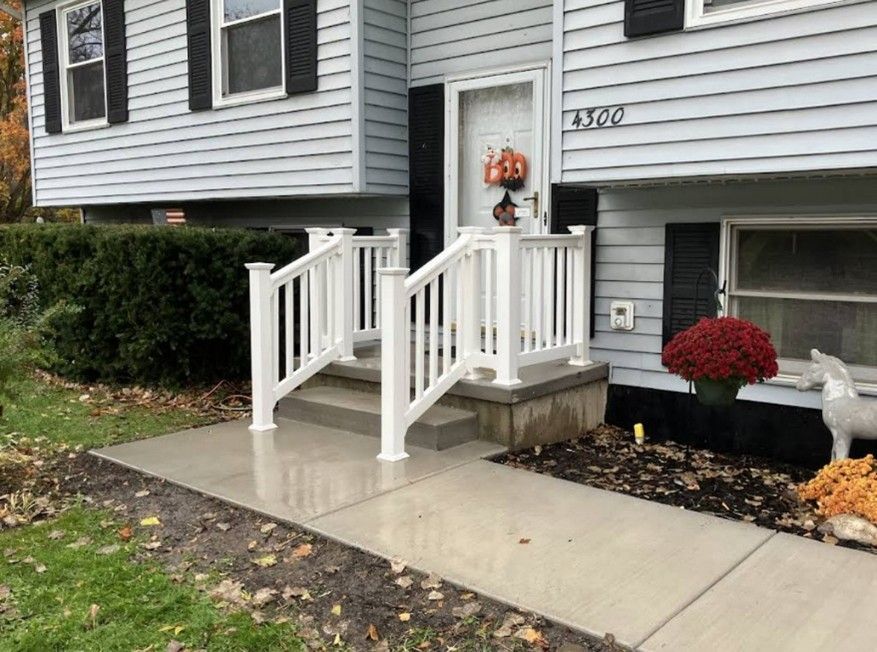 White railing on a concrete front porch of a house with light blue siding.