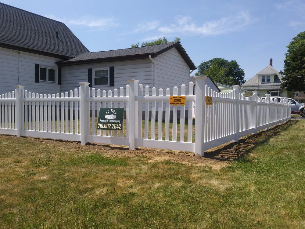 White vinyl picket fence installed around a yard beside a single-story house. White vinyl picket fence installed around a yard beside a single-story house.