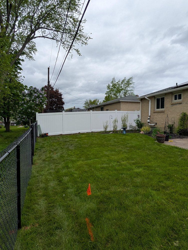 Backyard with green lawn, black chain-link fence, and white vinyl privacy fence. Backyard with green lawn, black chain-link fence, and white vinyl privacy fence.
