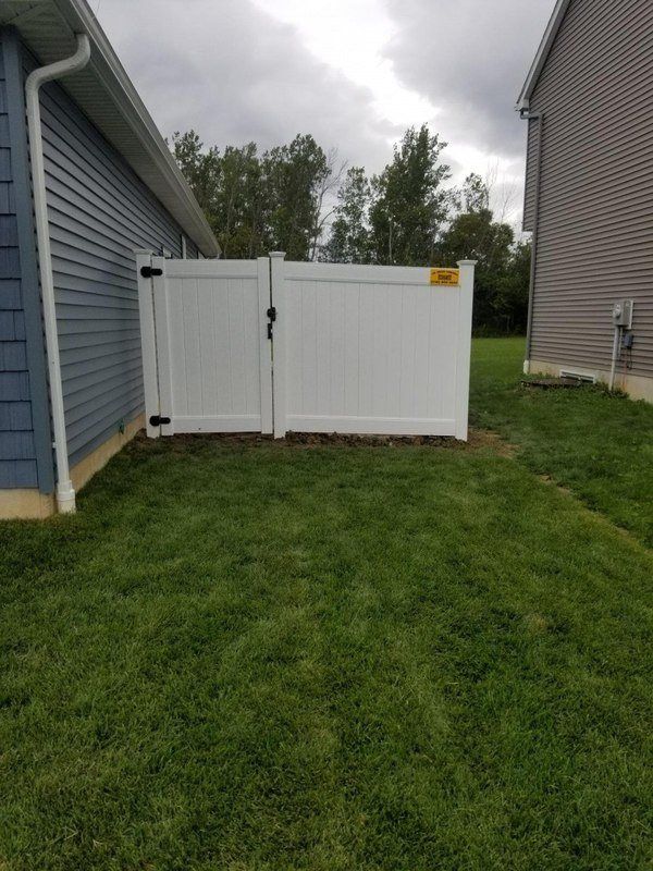 White vinyl fence between two houses on a grassy lawn; cloudy sky above.