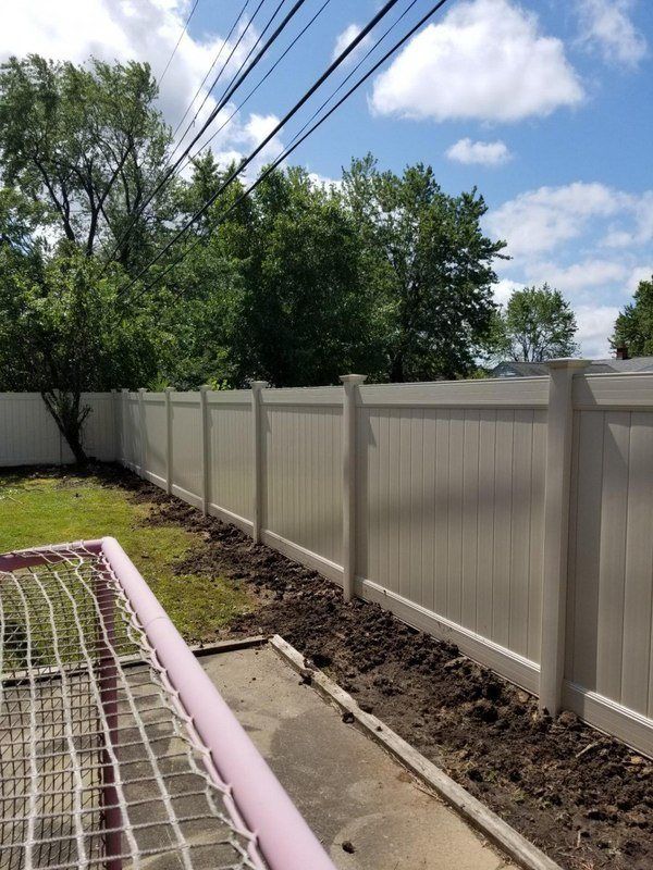 White vinyl fence in a backyard, with exposed dirt and grass. Power lines and trees in the background.