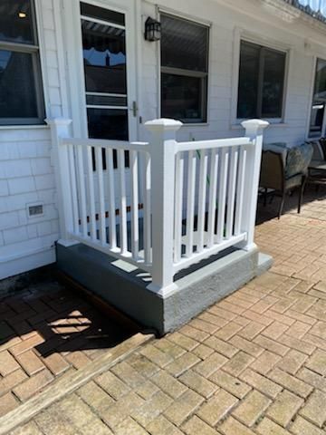 A white railing on a brick porch next to a white house.