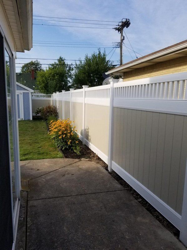 Backyard with a tan and white vinyl fence, green grass, a shed, and a concrete patio.