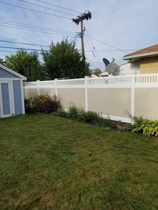 Backyard with green grass, tan and white vinyl fence, and blue shed.