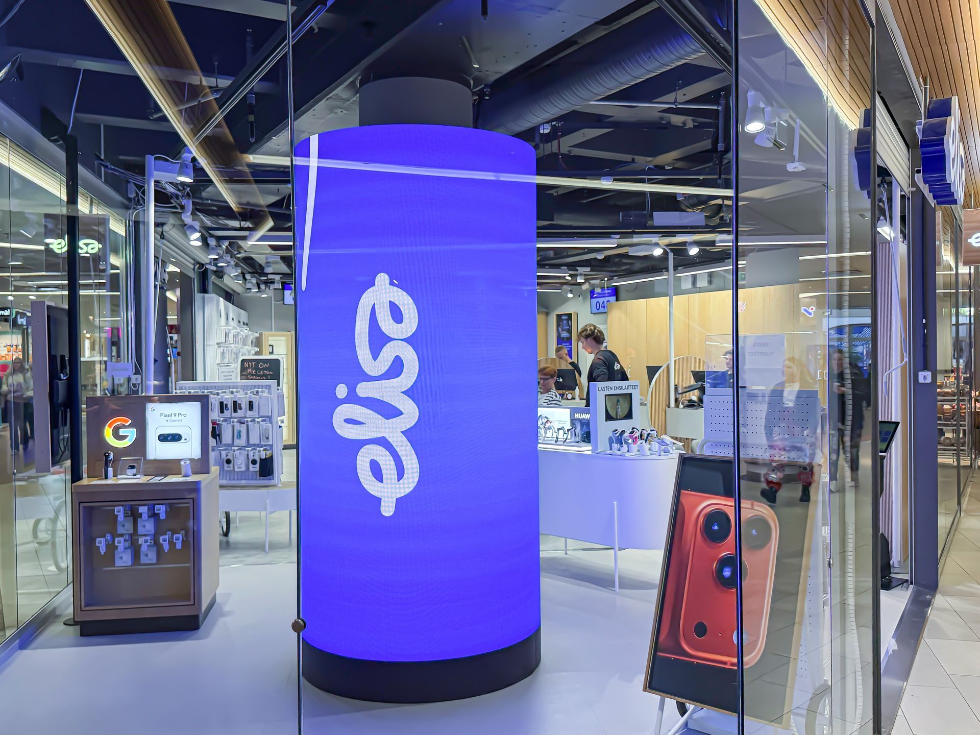 Elisa-myymälän sisätilat, joissa on suuri sininen sylinteri, jossa on logo. Henkilö seisoo valkoisen pöydän lähellä.