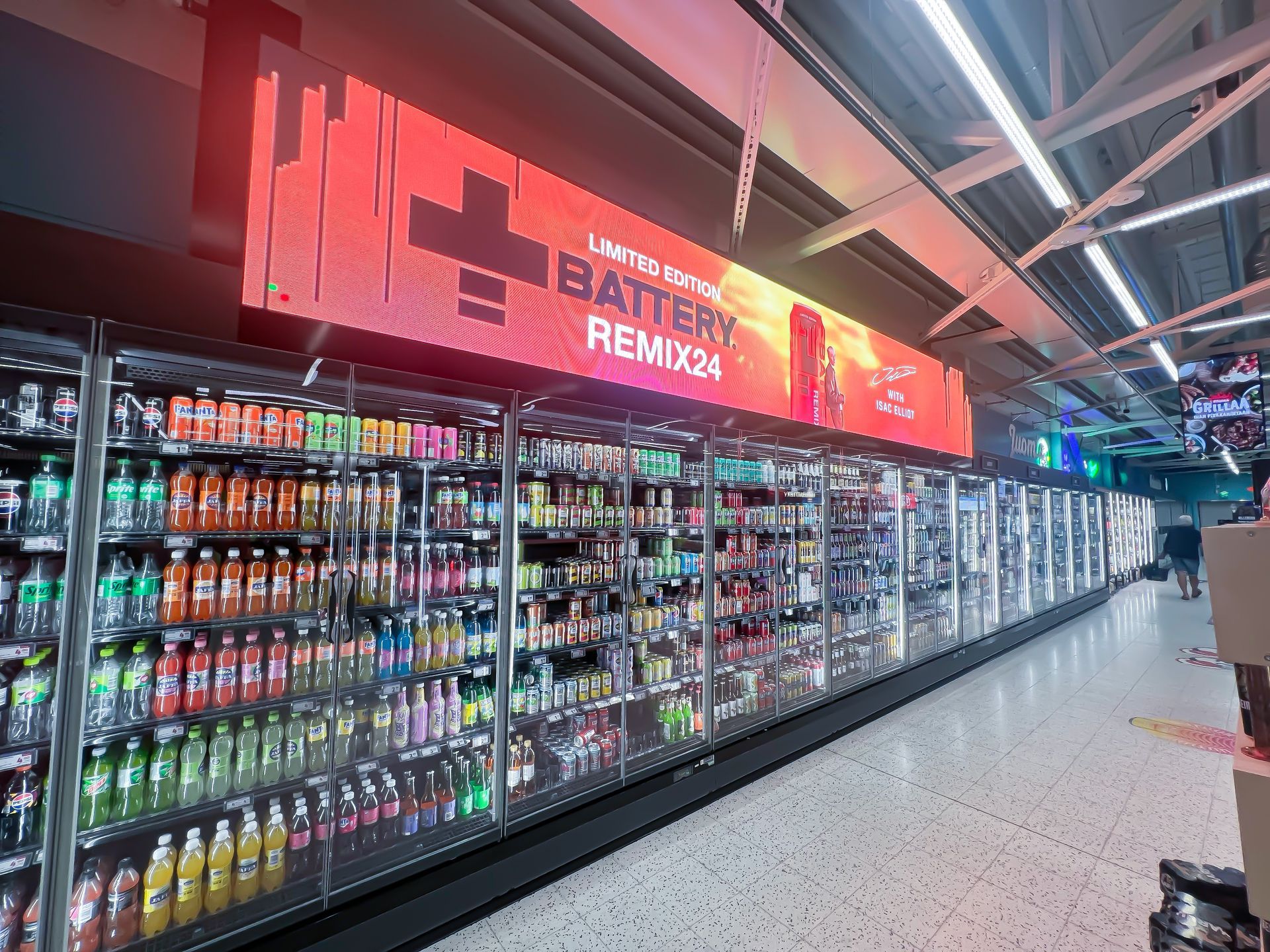 Värikkäitä juomia kylmässä juomahyllyssä. Kyltti Battery Remix34:lle. Myymälän sisätilat, kirkas valaistus.