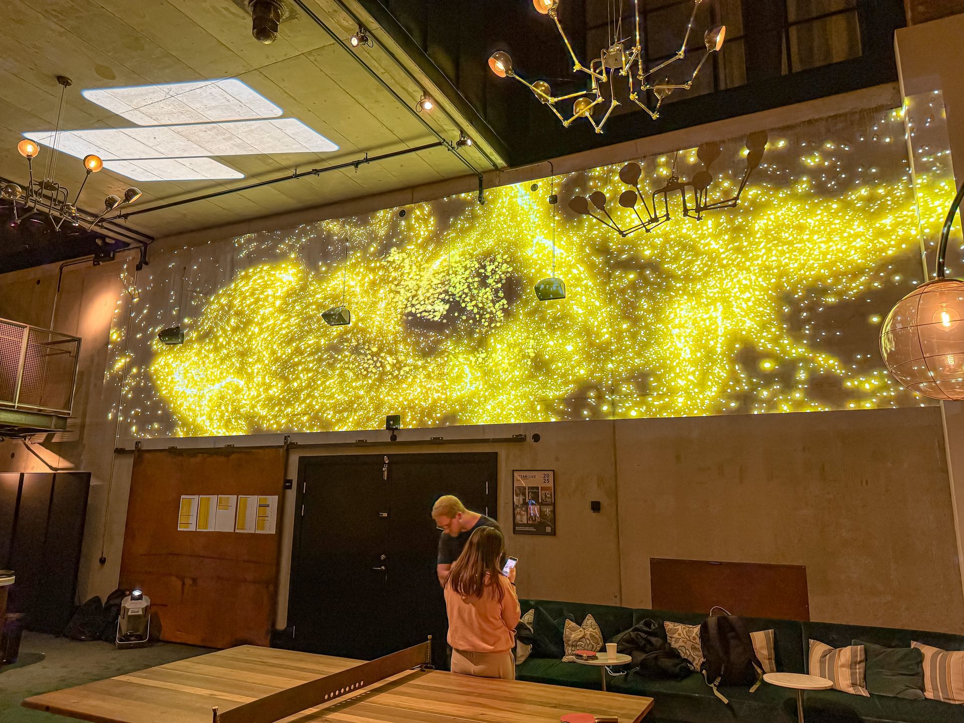 Ihmiset katsovat suurta kultaisten valojen seinäprojektiota hämärässä paikassa.