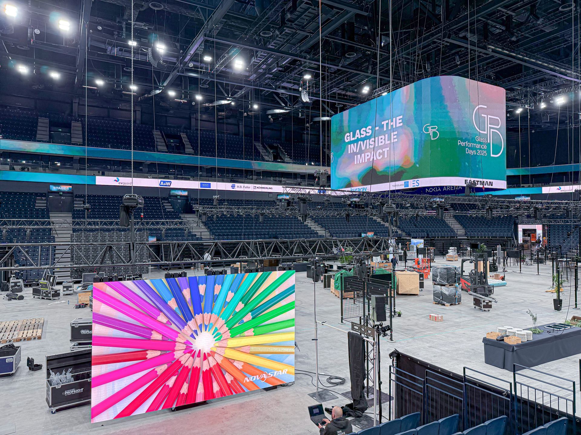 Tyhjä areenan sisätila, jossa on suuria LED-näyttöjä, joissa näkyy värikkäitä grafiikoita; paikalla rakennuslaitteita.