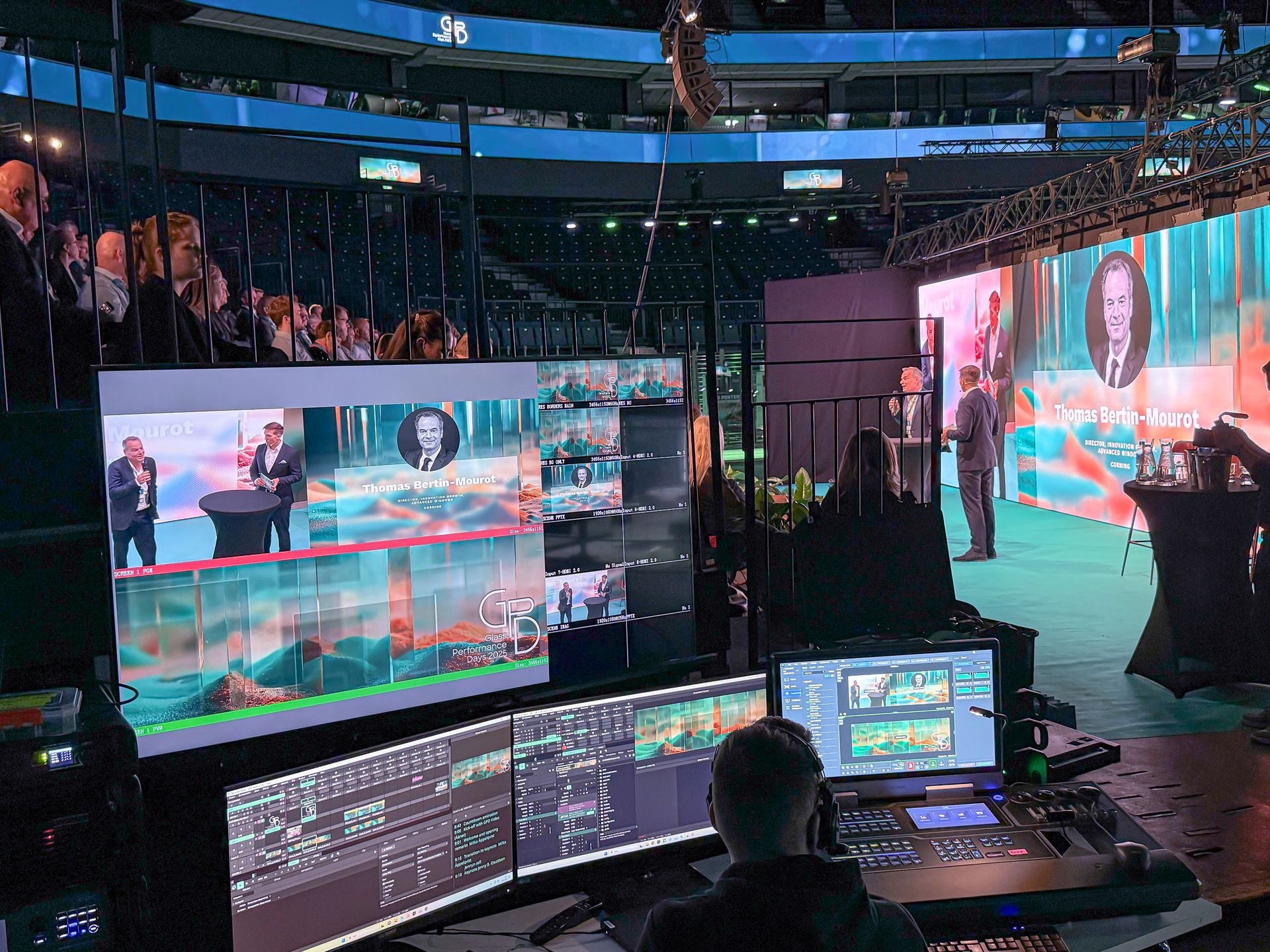 Tapahtuman asetukset: valvomoaseman miehistö valvoo näyttöjä, joilla näkyy areenan lavalla olevien puhujien ääni.