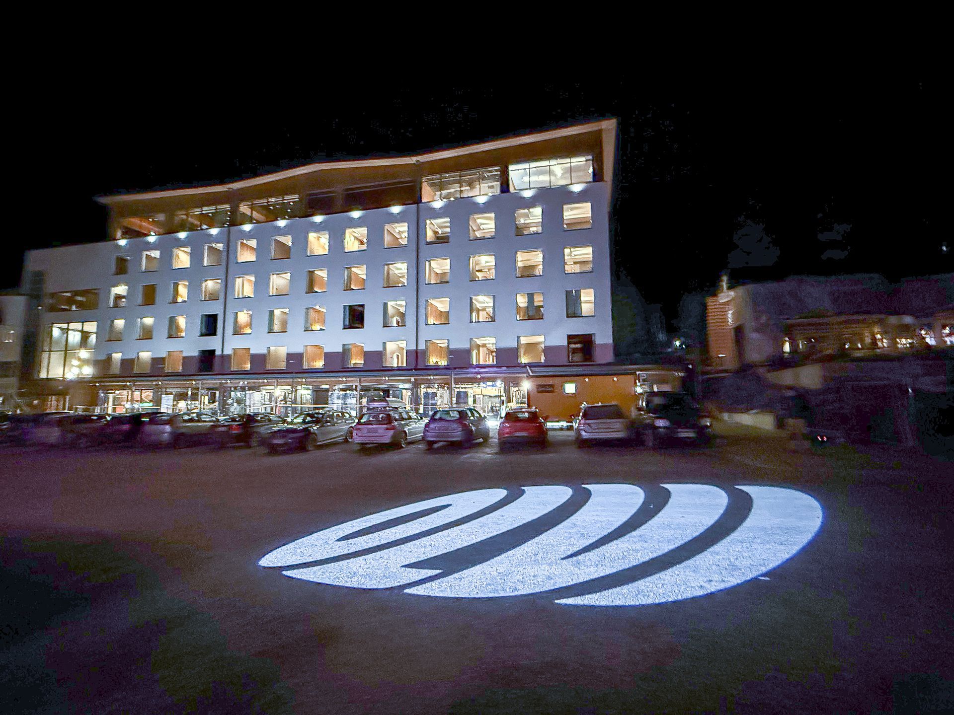 Hotelli valaistuna yöllä ja sen logo heijastettiin pysäköintialueelle.