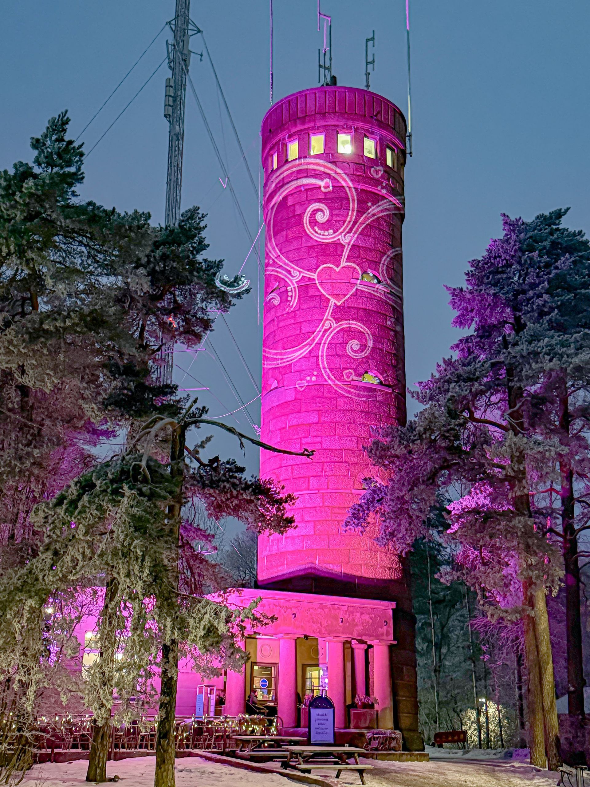 Vaaleanpunainen kivinen torni, jossa on sydän- ja kääröaihe. Puiden ympäröimä lumisessa ympäristössä.