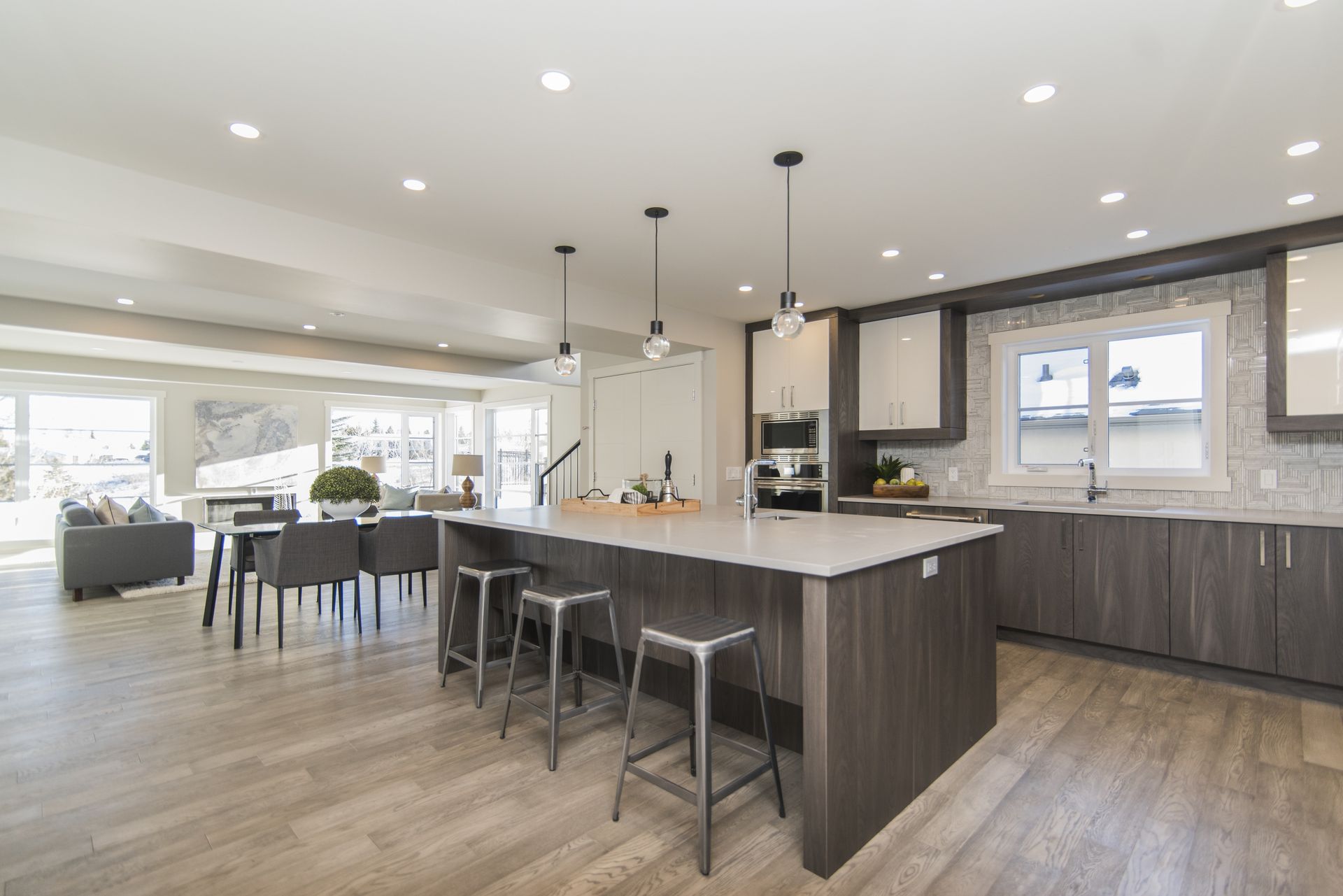 A modern kitchen with dark cabinetry, a central island with three metal stools, and an open-concept dining area.