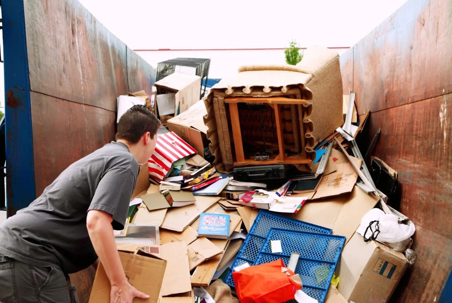 A man is looking at a pile of cardboard boxes in a dumpster.