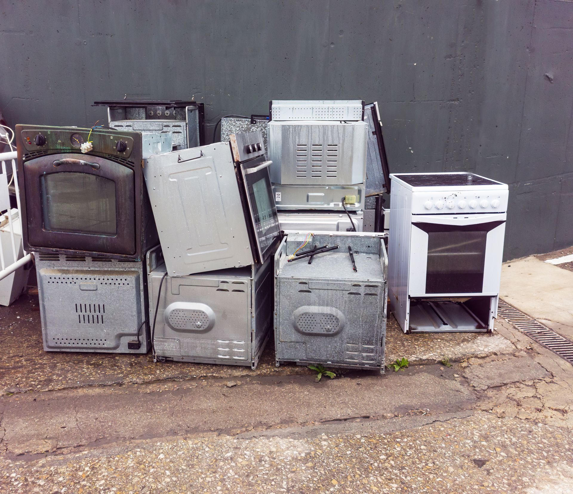 Pile of discarded ovens and cookers against a gray wall.