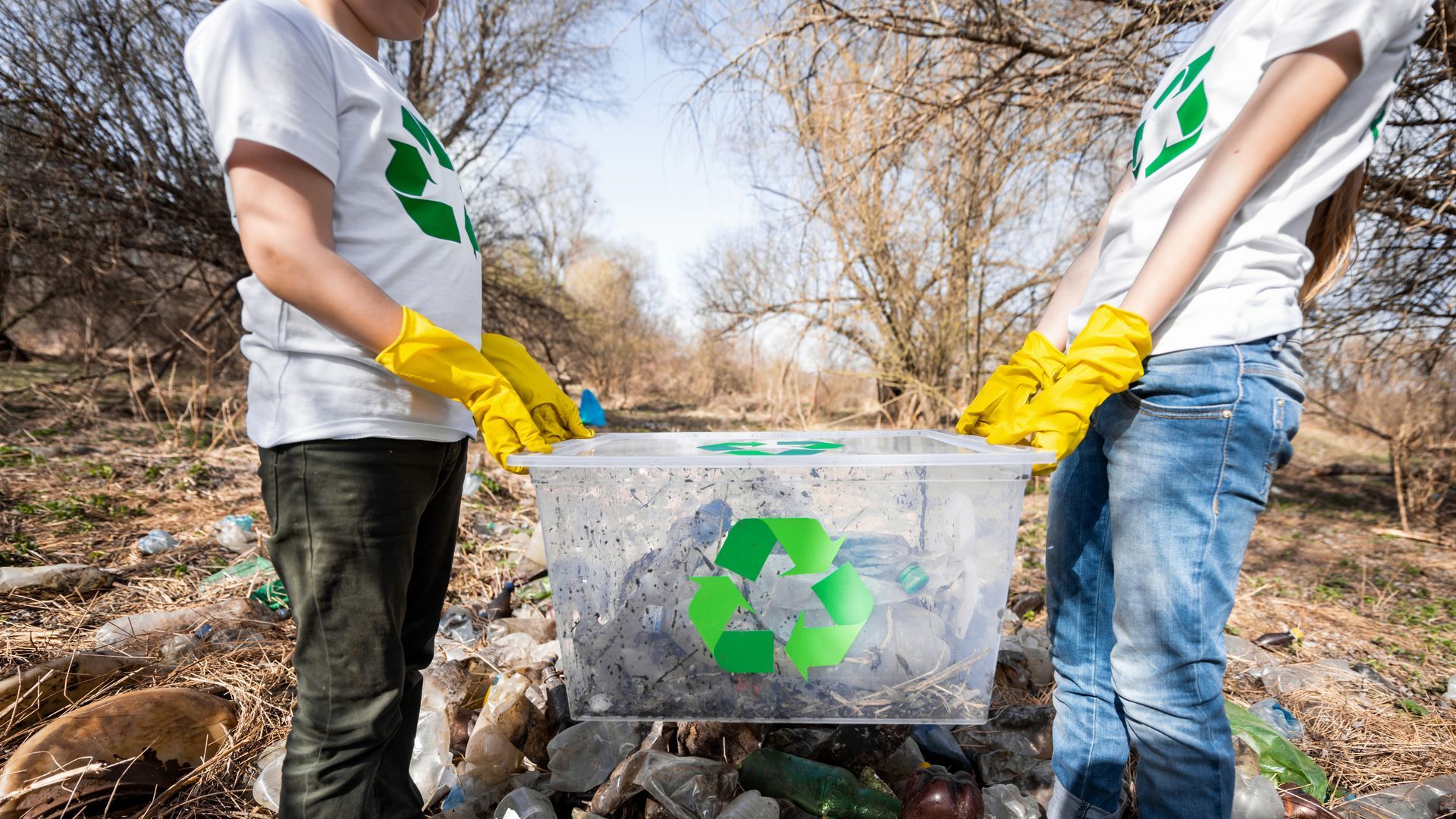 A man and a woman are holding a recycling bin in a park.