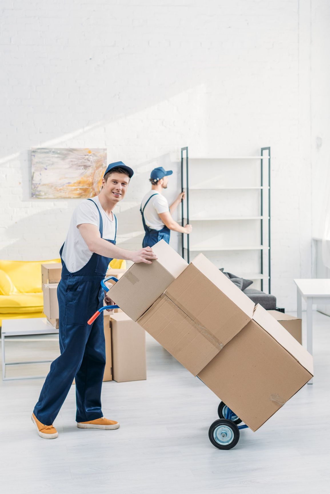 Two men are moving boxes on a dolly in a living room.