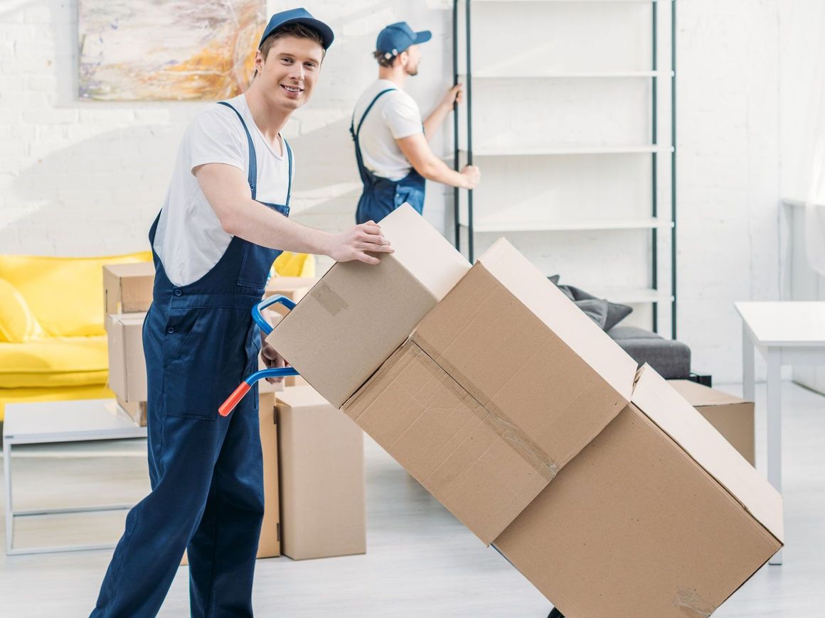 Two men are moving boxes on a dolly in a living room.