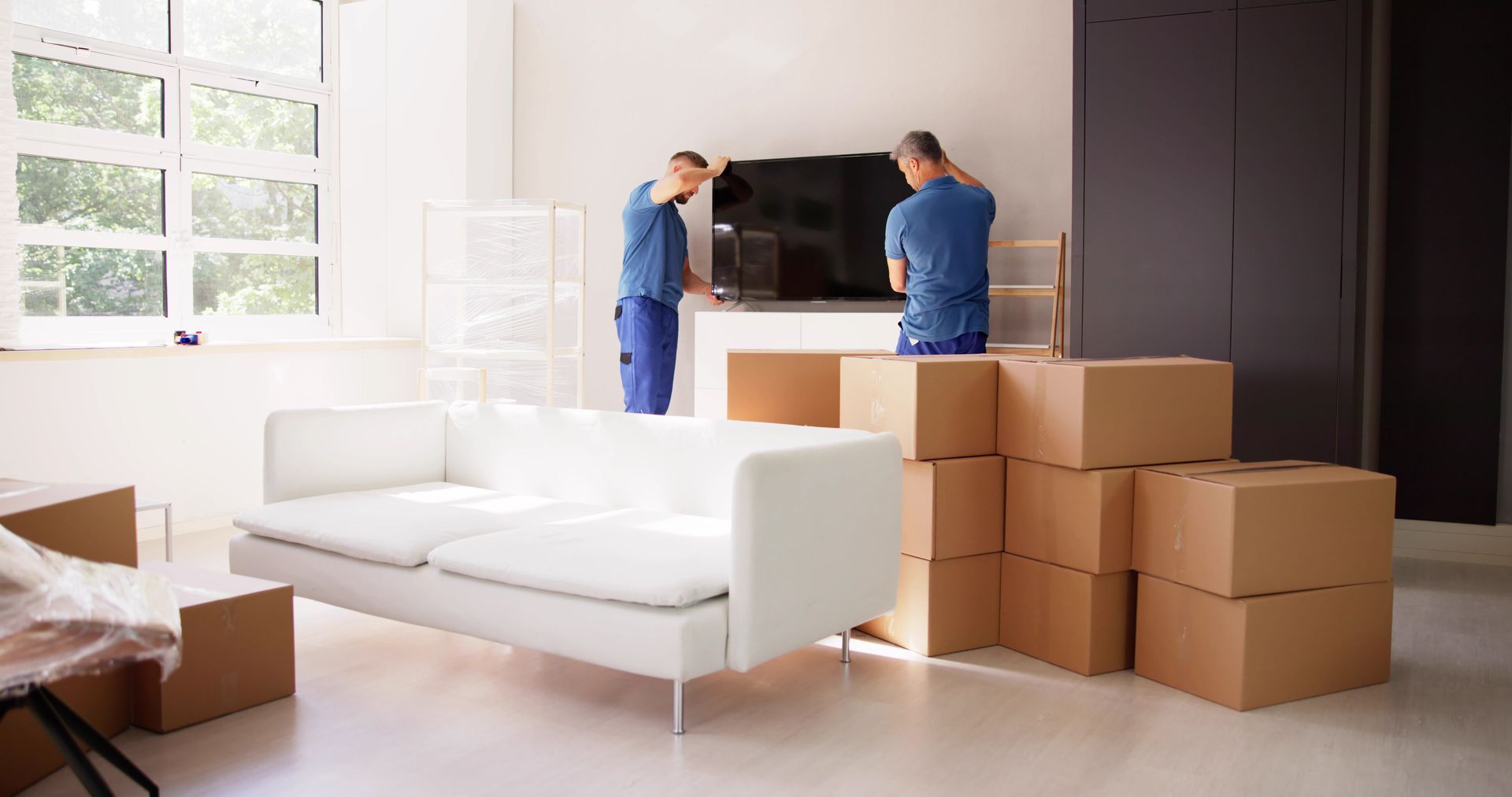 Two men are moving a television in a living room.