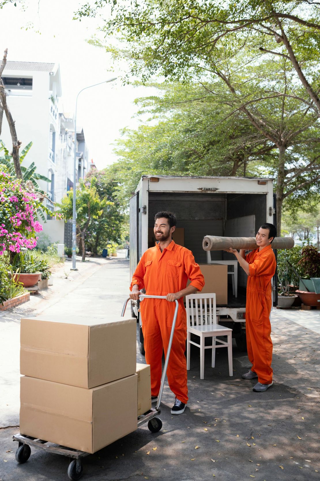 A man is pushing a cart full of boxes and a man is carrying a rug.